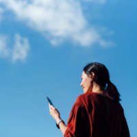 low angle portrait of young asian woman using smartphone against beautiful blue sky with cloudscapes, enjoying sunlight outdoors. lifestyle and technology - travel stock pictures, royalty-free photos & images