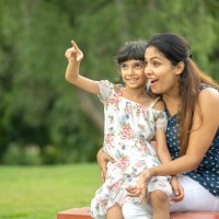 mère enjouée avec sa fille assise sur un banc contre des arbres luxuriants dans un parc - garden decoration photos et images de collection