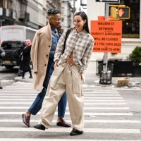 Mal Wright is seen waring a tan coat, jean top and pants and gold earrings with clear glasses with Rae Sada wearing a plaid shirt, tan pants and...