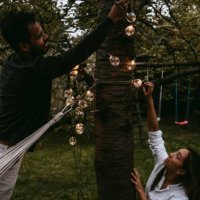 male and female friends hanging lighting equipment in backyard during dinner party - garden decoration stock pictures, royalty-free photos & images