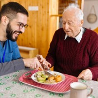 male care worker serving dinner to a senior man at his home - food stock pictures, royalty-free photos & images