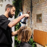 male hairdresser drying the hair of a client sitting in front of a mirror in a modern hairdressing salon. - hairstyle stock pictures, royalty-free photos & images