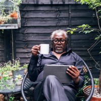 male professional holding mug looking at digital tablet while sitting on chair in backyard - garden decoration photos et images de collection