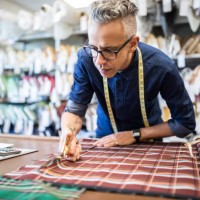 male tailor cutting a textile at workbench - fashion stock pictures, royalty-free photos & images