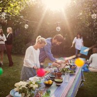 man and woman preparing food at dining table with friends in background during summer party - garden decoration stock pictures, royalty-free photos & images