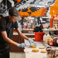 man, burger and fast food kitchen worker at counter with gloves, cooking and uniform at small business. restaurant, sandwich and cook with hamburger patty stack for lunch service with take away. - junk food stock pictures, ro