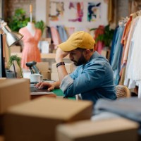 man, designer and laptop stress for fashion logistics in studio with boxes for shipping, supply chain or deadline. male person, problem and boutique store for online order, distribution or package - fashion stock pictures, ro