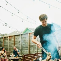 man grilling steaks for friends at backyard barbecue during party - garden decoration photos et images de collection