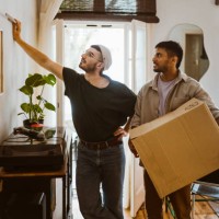 man holding cardboard box while talking to boyfriend looking at painting on wall - home decoration stock pictures, royalty-free photos & images