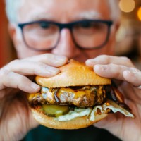 man holding delicious fresh flame grilled burger in restaurant - junk food stock pictures, royalty-free photos & images