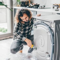 man in a kitchen repairing a washing machine. - home decoration stock pictures, royalty-free photos & images