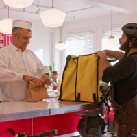 man in a white button down shirt packs order for delivery person in a 1950s styled diner - junk food stock pictures, royalty-free photos & images