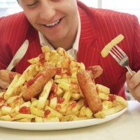 man in red suit eating large plate of sausages and chips - junk food stock pictures, royalty-free photos & images