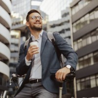 man leaning on bicycle and holding cup of coffee on the city streets - junk food stock pictures, royalty-free photos & images