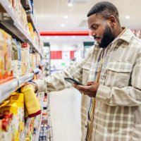 man looking at smartphone while choosing items in supermarket - food stock pictures, royalty-free photos & images