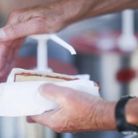man putting tomato sauce on a hotdog - junk food stock-fotos und bilder