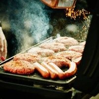 man seasoning burgers and hot dogs on barbecue - food fotografías e imágenes de stock