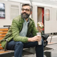man sitting on a bench at the train station with sandwich and hot drink - junk food stock pictures, royalty-free photos & images