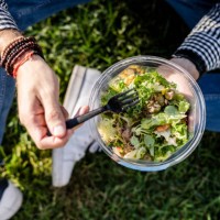 man sitting on a meadow eating mixed salad, partial view - junk food stock pictures, royalty-free photos & images