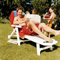 man sitting on a sun lounger with a newspaper is surprised by two boys with water-guns - garden decoration photos et images de collection