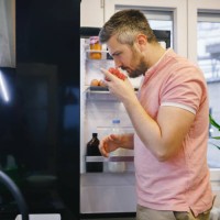 man standing in the kitchen, holding a box of cherry tomatoes and smelling it - food stock pictures, royalty-free photos & images