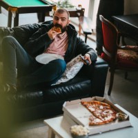 man watching tv and eating take-out pizza at home - junk food stock pictures, royalty-free photos & images