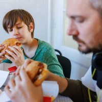 man with headphones and his preadolescent son having take out burgers at the table - junk food stock pictures, royalty-free photos & images