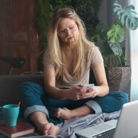man with long hair and beard sitting on sofa bed looking at smartphone - fashion stock pictures, royalty-free photos & images