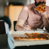 man working from home eating take-out pizza and using a laptop - junk food stock pictures, royalty-free photos & images