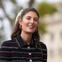 Maria de la Orden wears a bow tie hair bun, golden earrings, a dark blue red and white striped long tweed dress, outside Chanel, during the...