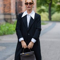 Maria Wos wears black coat, white blouse, Hermes bag, Holzweiler sunglasses, silver earrings at Oslo Fashion Week 2024 on August 27, 2024 in Oslo,...