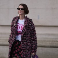 Marianne Theodorsen is seen wearing black sunglasses, long pearl earrings, a white t-shirt with the Chanel logo in pink, a long pink and black plaid...