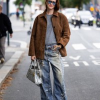 Marianne Theodorsen wears brown wild leather jacket, denim jeans with print, blue bag, grey short at Oslo Fashion Week 2024 on August 27, 2024 in...