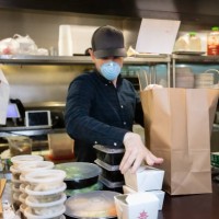 masked and gloved man in restaurant kitchen packaging food for delivery during covid-19 outbreak - junk food stock pictures, royalty-free photos & images