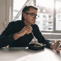 mature businessman checking cell phone during lunch break in office - junk food stock pictures, royalty-free photos & images