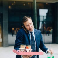 mature businessman talking on mobile phone while carrying food and drinks in city - junk food stock pictures, royalty-free photos & images