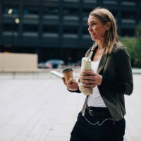 mature businesswoman carrying food and drink with laptop while walking on footpath in city - junk food stock pictures, royalty-free photos & images