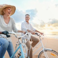 mature couple cycling on the beach at sunset or sunrise. - travel stock pictures, royalty-free photos & images