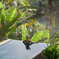 mature fit asian woman relaxing on edge of infinity pool, admiring jungle view with early morning mist - travel stock pictures, royalty-free photos & images
