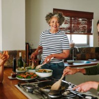 mature women laughing while cooking together in the kitchen of their vacation rental - food stock pictures, royalty-free photos & images