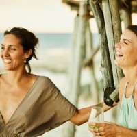medium shot of woman laughing with friends on beach at tropical resort at sunset - fashion stock pictures, royalty-free photos & images