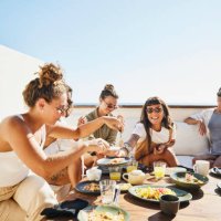 medium wide shot of smiling female friends sharing breakfast on deck of luxury suite at tropical resort - food stock pictures, royalty-free photos & images