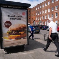 Members of the public pass a bus stop advertisement for McDonald's, the international fast food restaurant, and their new barbeque quarter pounder on...