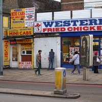 Members of the public walk past a mini-cab kiosk and a fst food fried chicken outlet near Lewisham high street on December 5, 2012 in London,...