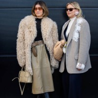 Michelle Fleur wears beige faux fur jacket, high waisted skirt with brown belt, bag, black top, black boots, sunglasses & Elise Bak wears grey...