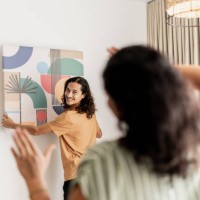 mid adult man asking his wife for help to put the frame on the wall in living room at new house - home decoration stock pictures, royalty-free photos & images