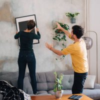 mid adult man guiding girlfriend in hanging picture frame on wall at new home - home decoration stock pictures, royalty-free photos & images