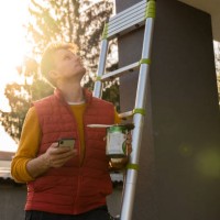 mid adult man holding paint equipment and smart phone looking at apartment - home decoration stock pictures, royalty-free photos & images