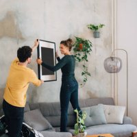 mid adult man passing picture frame to girlfriend against wall at new home - home decoration stock pictures, royalty-free photos & images