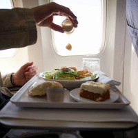 mid adult man sitting at airplane, adding mustard to salad - food stock pictures, royalty-free photos & images